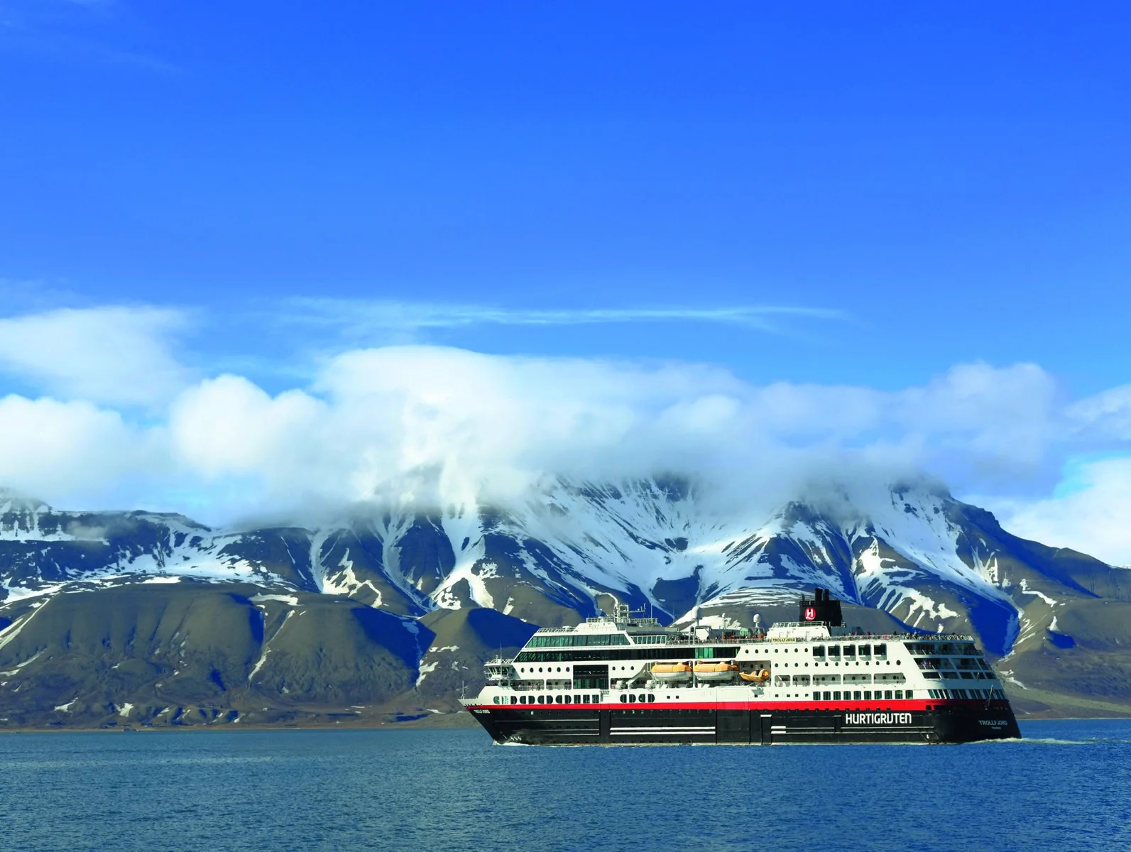 Hurtigrutens fartyg framför snöklädda berg på Svalbard